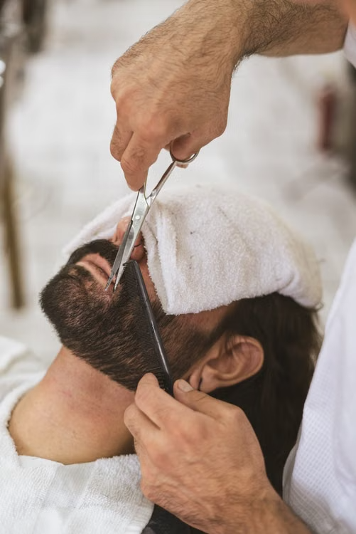 Barber trimming a client's beard with scissors and a comb at Express Cuts