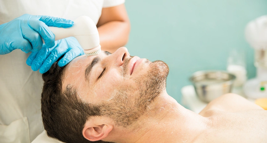 Client relaxing while a facial cleansing brush is used on his forehead